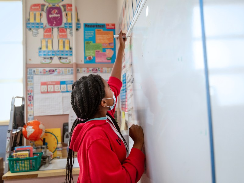 A student writes on a board at Stege Elementary School in Richmond on Feb. 6, 2023. Photo by Shelby Knowles for CalMatters