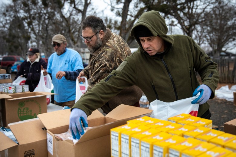 Volunteers Jeff Mummy (right), Michael Merrill (center) and others prepare bags of food for distribution by the Trinity County Food Bank at the Trinity County Fairgrounds on Feb. 8, 2023. Photo by Martin do Nascimento, CalMatters