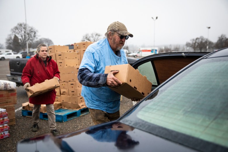 Volunteers Terry Scovil (center), and Shendi Klopfer load the car of a community member with food from the Trinity County Food Bank at the Trinity County Fairgrounds on Feb. 8, 2023. Photo by Martin do Nascimento, CalMatters