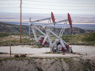 Two white and red oil pumps next to each other on a small dirt hill overlooking several farming fields in the distance.