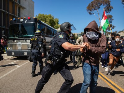 A University of California campus police officer pushes a pro-Palestinian protester away from a moving San Diego Sheriff's bus with arrested protesters onboard at UC San Diego in San Diego on May 6, 2024. Photo by Adriana Heldiz, CalMatters