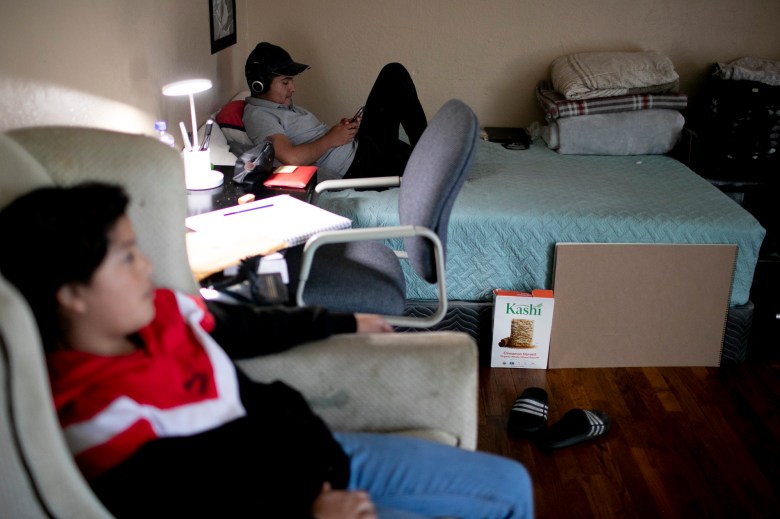 Eduardo sits on his bed while checking his phone in the living room of the home he shares with his siblings and nieces. Photo by Anne Wernikoff, CalMatters