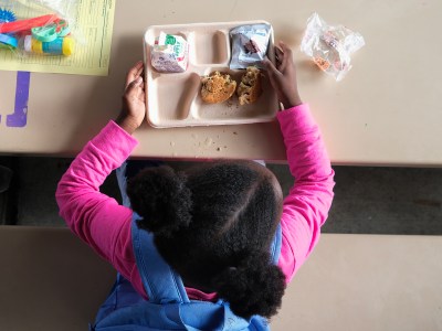 A young girl sits down to eat free breakfast at Rosa Parks Elementary School in San Diego on June 14, 2024. San Diego Unified School District is partnering with local organizations to offer free meals to families and students during the summer. Photo by John Gastaldo for CalMatters