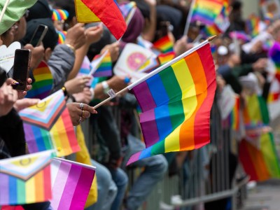 A person holding a Pride flag while lined-up behind a barricade during a parade.