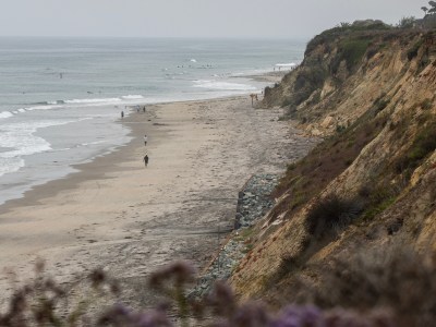 People walk a long a beach nestled between the ocean and a bluff during a foggy day in Del Mar.