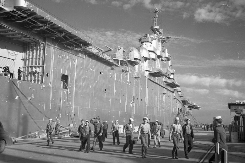 A black and white photo from 1947 of servicemen walking away from a large navy ship Hunters Point Naval Shipyard in San Francisco.