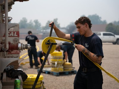 Chris Castleman, a Cal Fire firefighter, rolls up a fire hose on a fire truck at the Park Fire command post in Chico on Aug. 2, 2024, shortly after returning from fighting the nearby flames. Photo by Florence Middleton, CalMatters