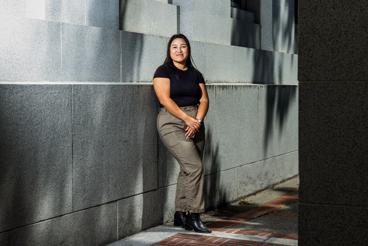 A person in grey slacks, black boots and a black shirt stands in the corridor between two buildings. Dramatic light causes and interesting contrast of light and shadows.