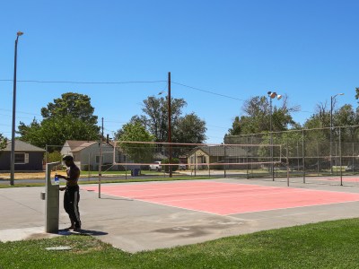 A person with pants, but no shirt, fills their water bottle during a hot day at a water station at a tennis court.