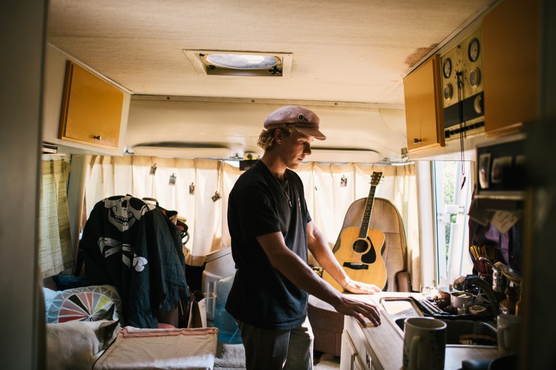 A man stands in the center of an RV, staring at the countertop near the entrance.