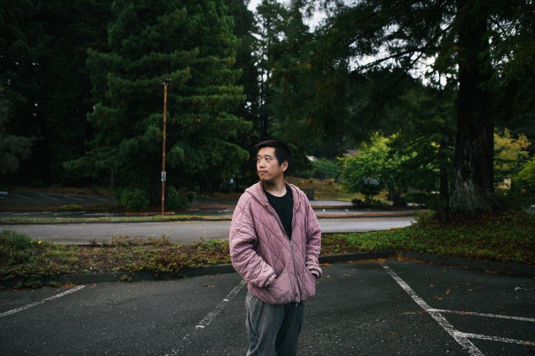 A man in a jacket stands in an empty parking lot of a college campus