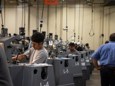 A row of students wearing safety goggles working on machines in a mechanical classroom.