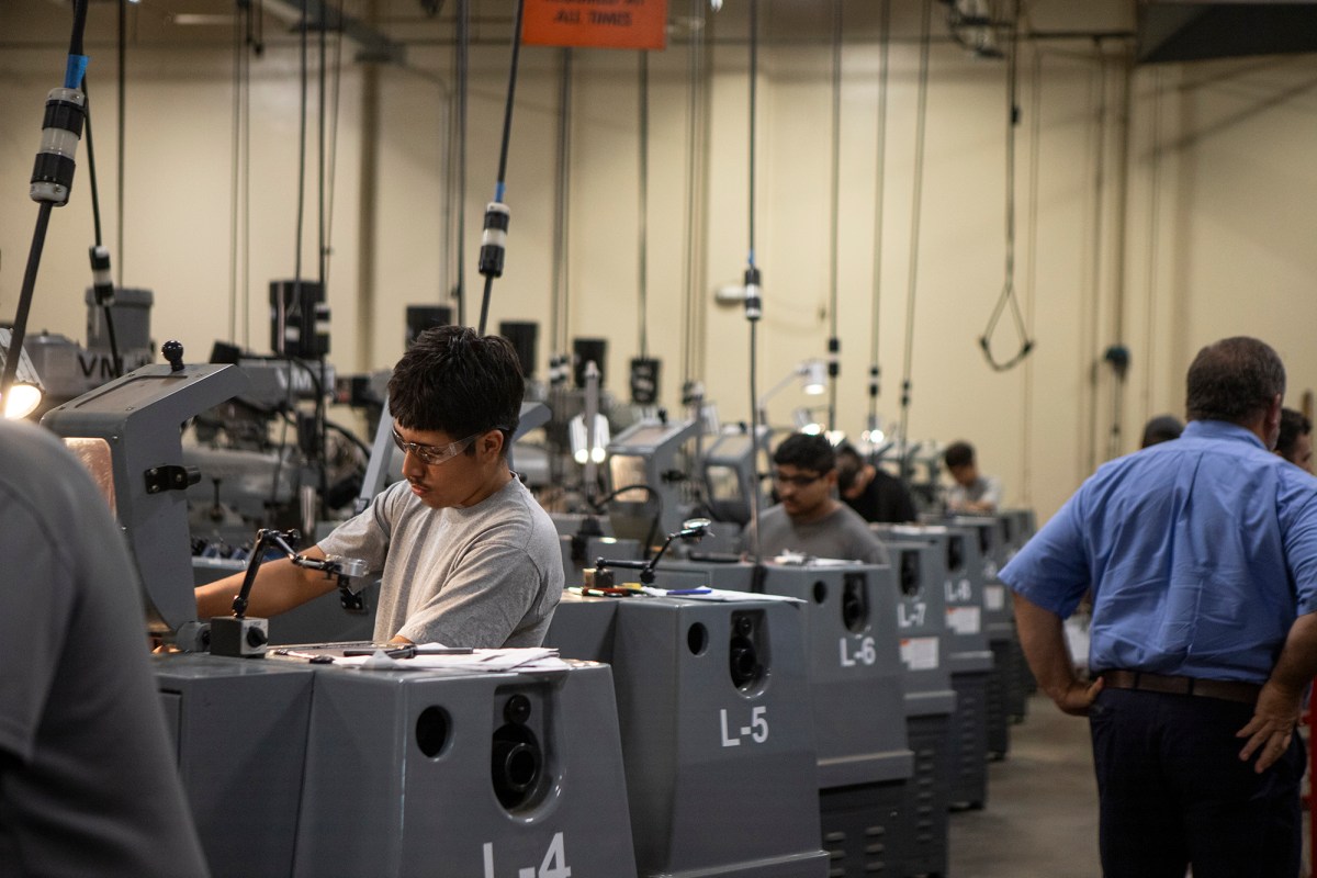 A row of students wearing safety goggles working on machines in a mechanical classroom.