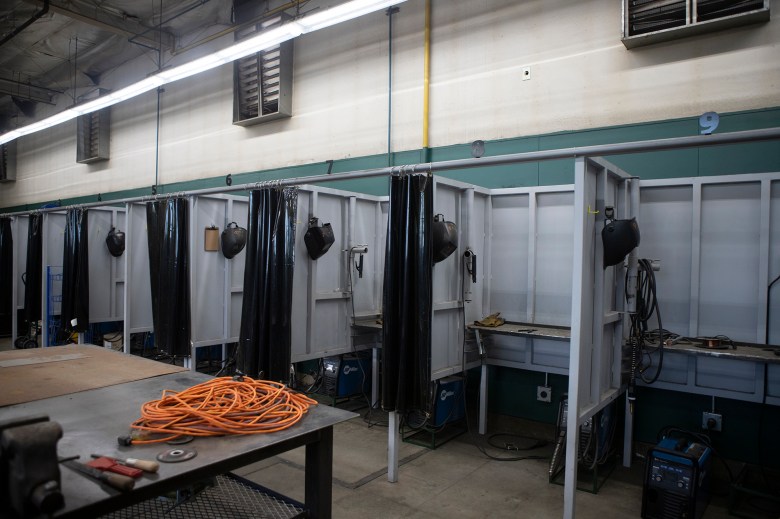 A row of empty welding workstations for high school students with welding masks hanging in every station.