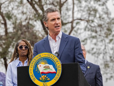 Gov. Gavin Newsom, wearing a blue suit and white shirt, stands behind a black podium with the California state seal on it during a press conference.