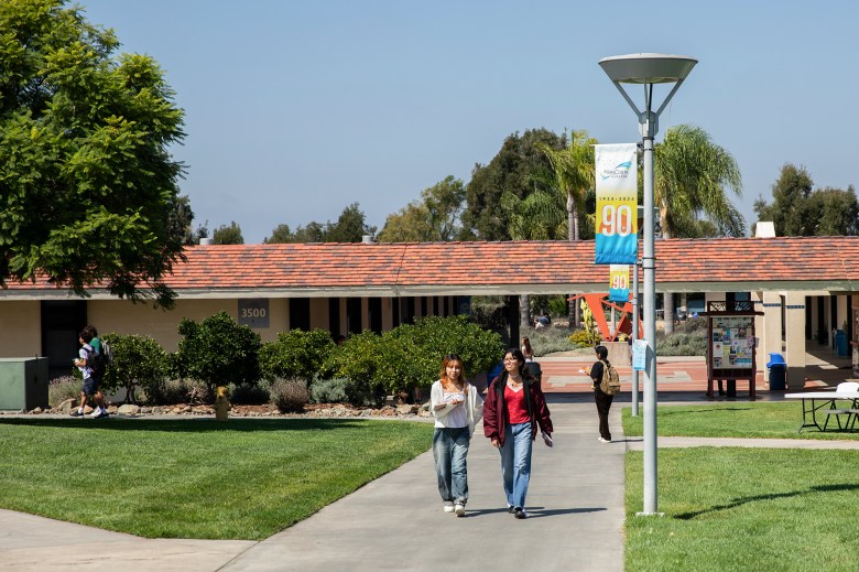 Students walking through a college campus on a sunny day along a walkway.