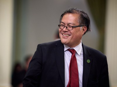 A close-up view of a lawmaker wearing a black suit and red tie as he smiles and looks to this right.