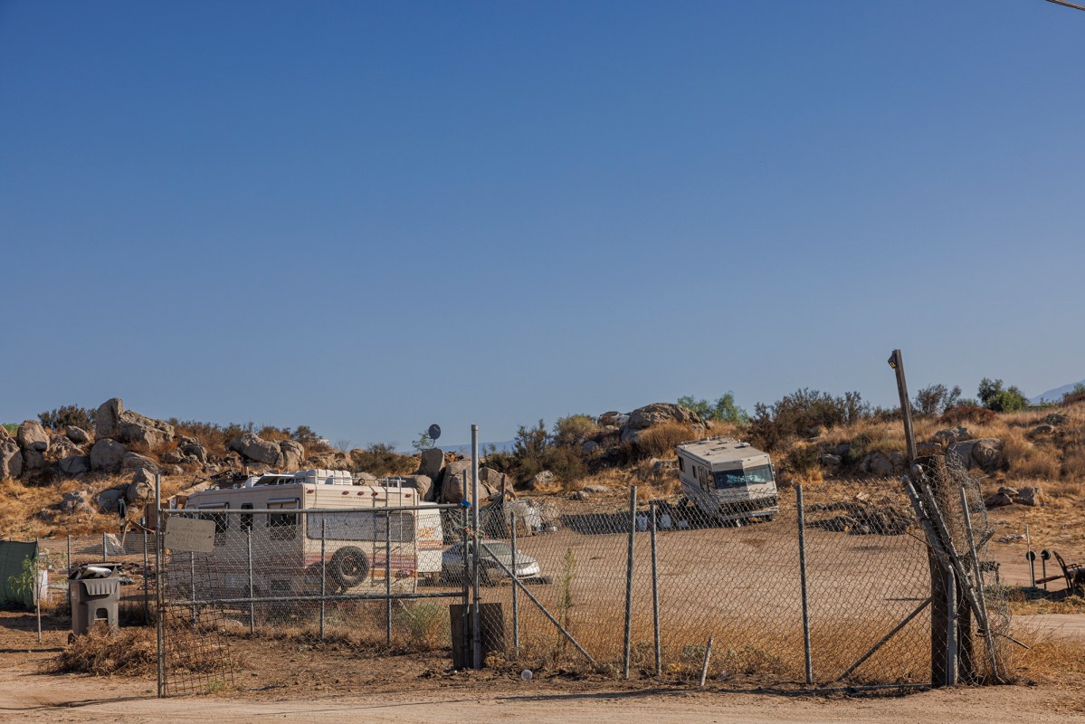 View of a trailer community on an unpaved road inside a fenced in area.