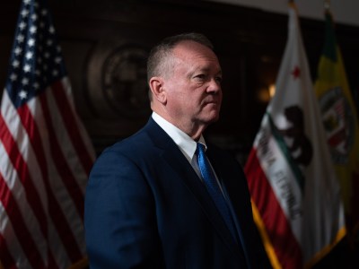 A ray of light shines on the right side of a person's face as they stand in front of an American flag and California flag during a press conference.