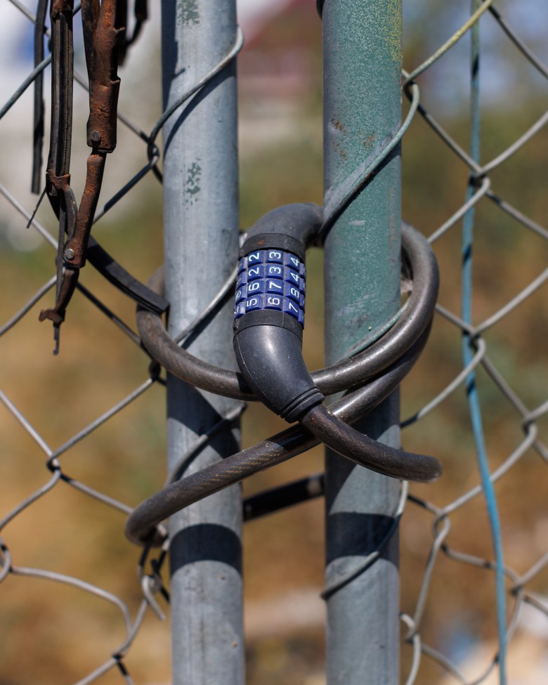 A close-up view of a blue coded lock wrapped around two ends of a fence.