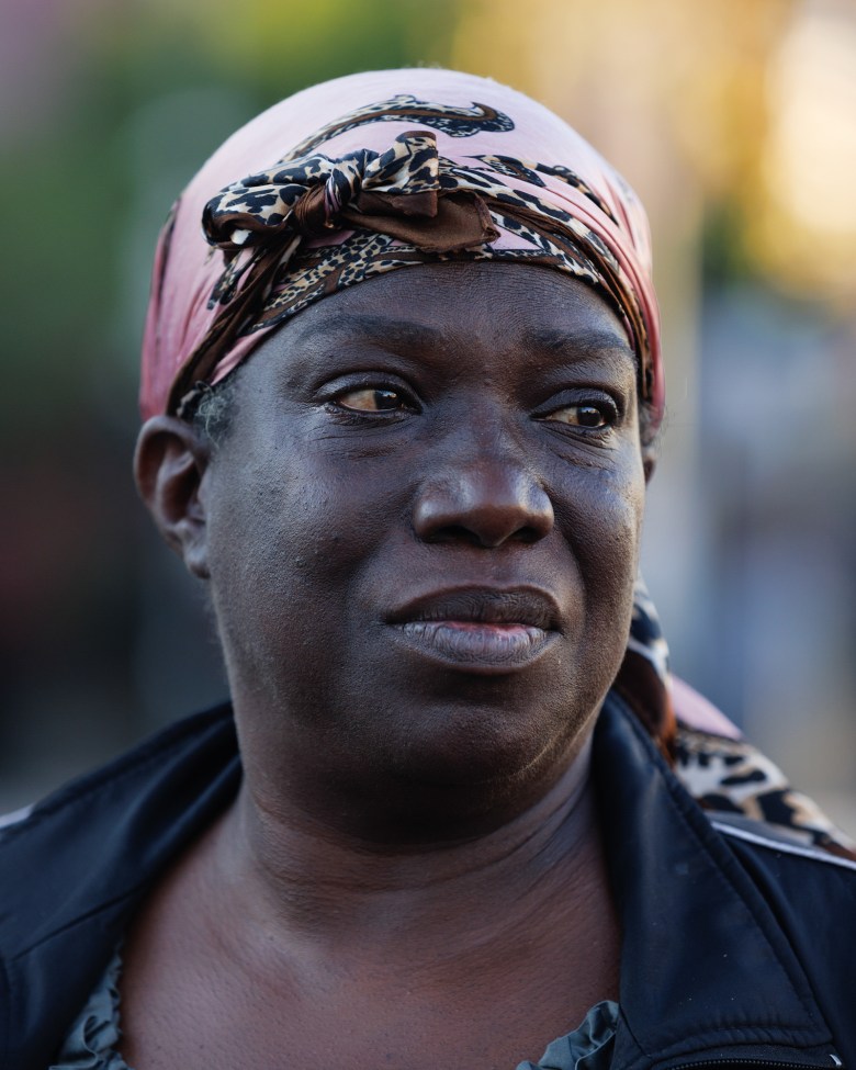 A close-up view of a woman's face as she wears a pink leopard-patterned head wrap and looks towards their left side.