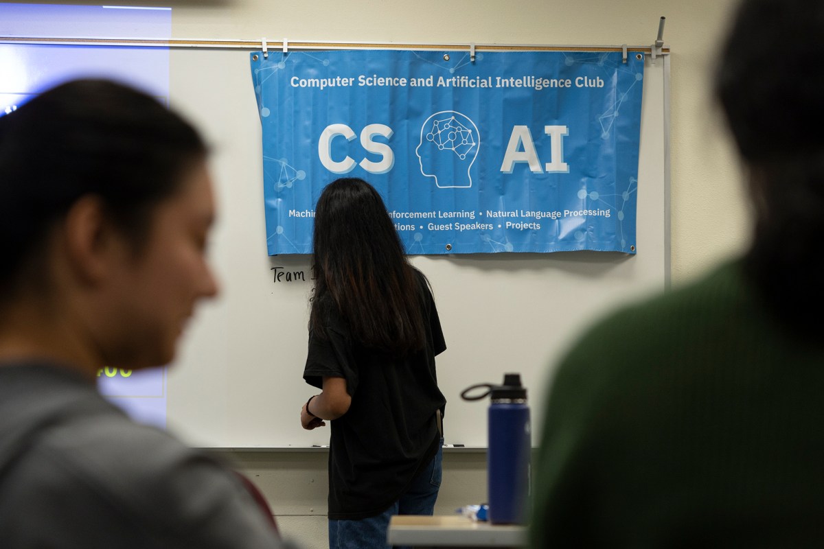 A student writing on a white board under a banner for the AI club in a classroom.