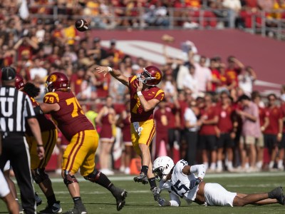 A football player throws a football during a play in a college football stadium.