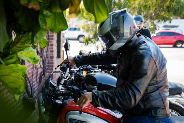 A man in a helmet starting up his motorcycle in a parking lot near a brick wall.