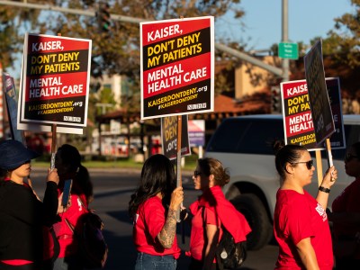 A line of protestors holding signs and marching in front of a hospital.