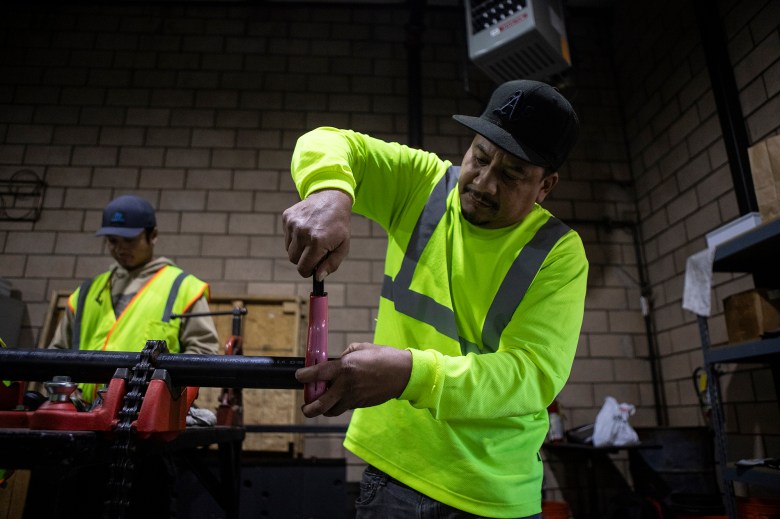 A person uses a tool to cut a section of pipe inside of a workshop