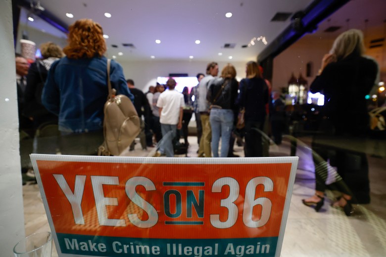 A sign leaned against a glass reads "YES on 36 Make Crime Illegal Again." People stand in the background, out of focus.