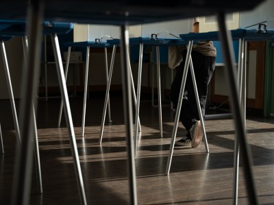 A close-up view of a person's checkered pattern shoes as they lean over a voting booth at a vote center.