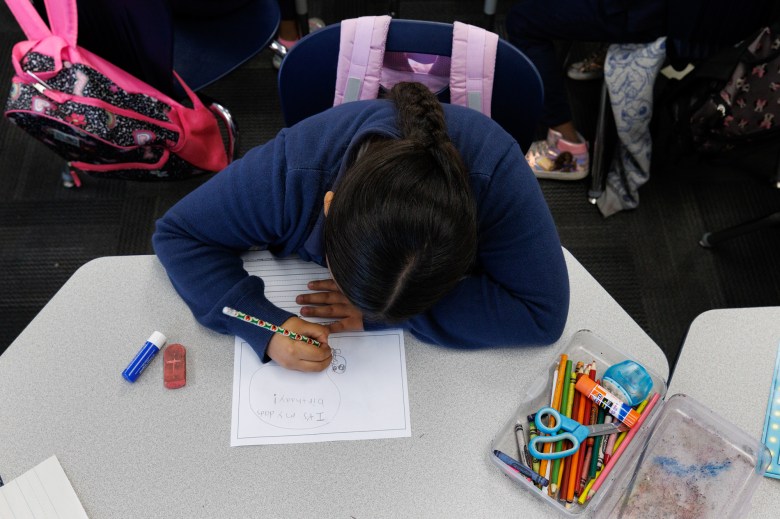 An over-head view of a student wearing a blue jacket and sitting in from of a desk and they write on a worksheet.