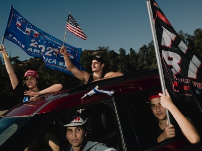 People wave flags in support of President-elect Donal trump while riding in a red car during a rally.