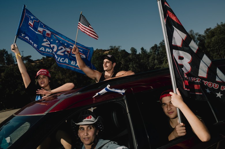 People wave flags in support of President-elect Donal trump while riding in a red car during a rally.