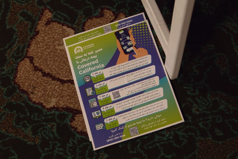 Two flyers with information written in Arabic about the Covered California program lay on a carpeted floor of a library.