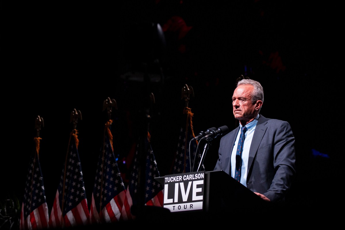 A person stands on stage at a podium with microphones next to a row of American flags.